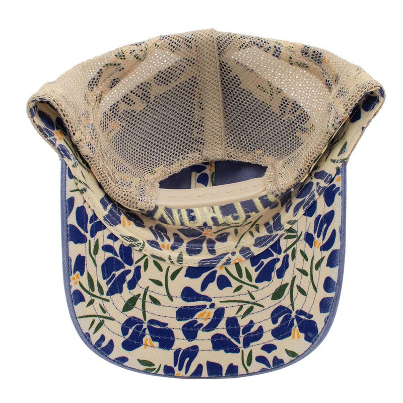 Underside of a baseball cap featuring a beige mesh back and a curved brim with a blue, green, and yellow floral pattern.